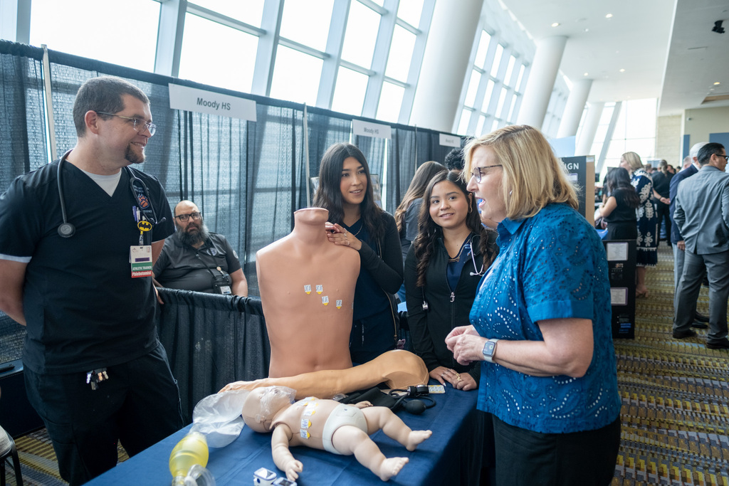 People stand around a table with a medical dummy, a baby dummy, and other items.