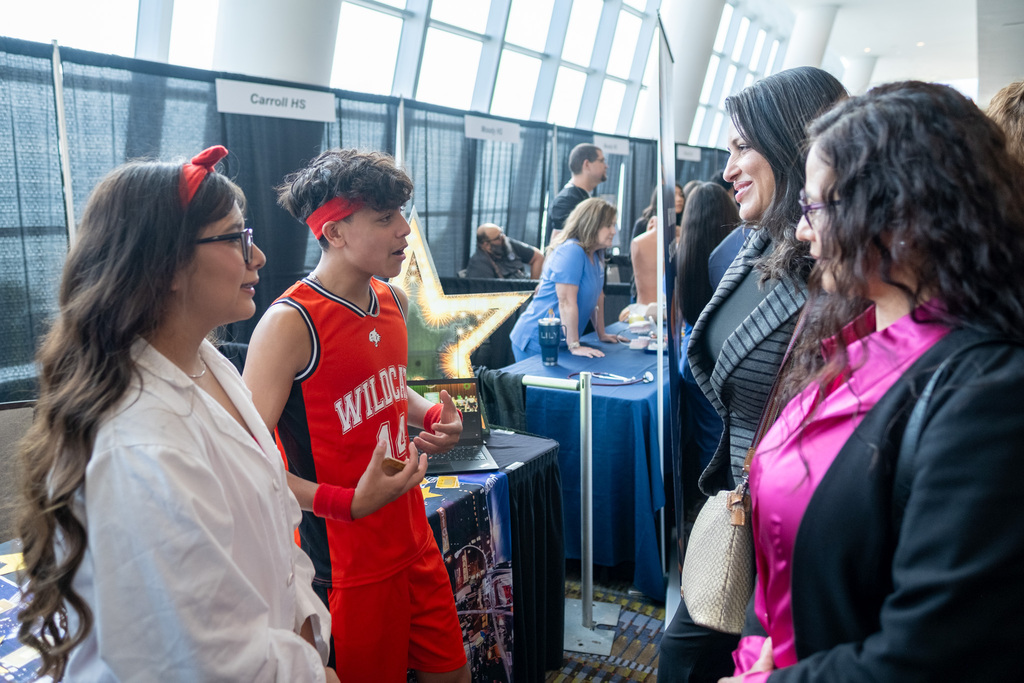 A group of people, including a man in a basketball uniform, converse in a convention center.