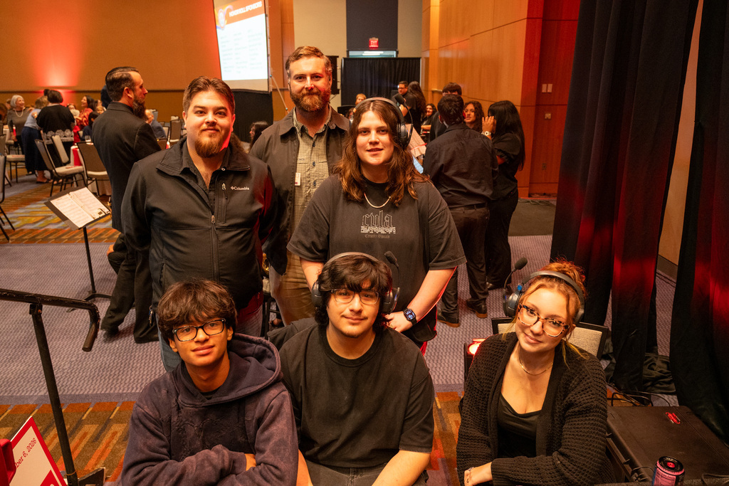 A group of people, four men and two women, pose for a photo in an indoor venue.
