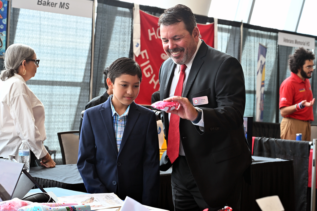 A man in a suit showing items to a young boy in a suit at a booth.