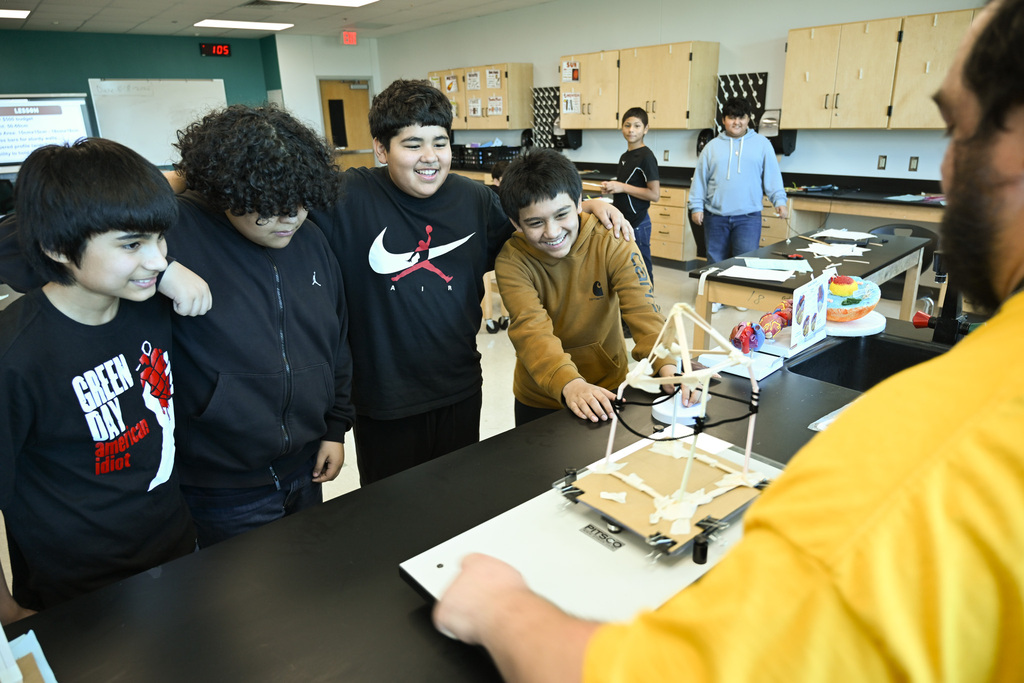 Five students in a science lab. One student is working on a project while others look on.