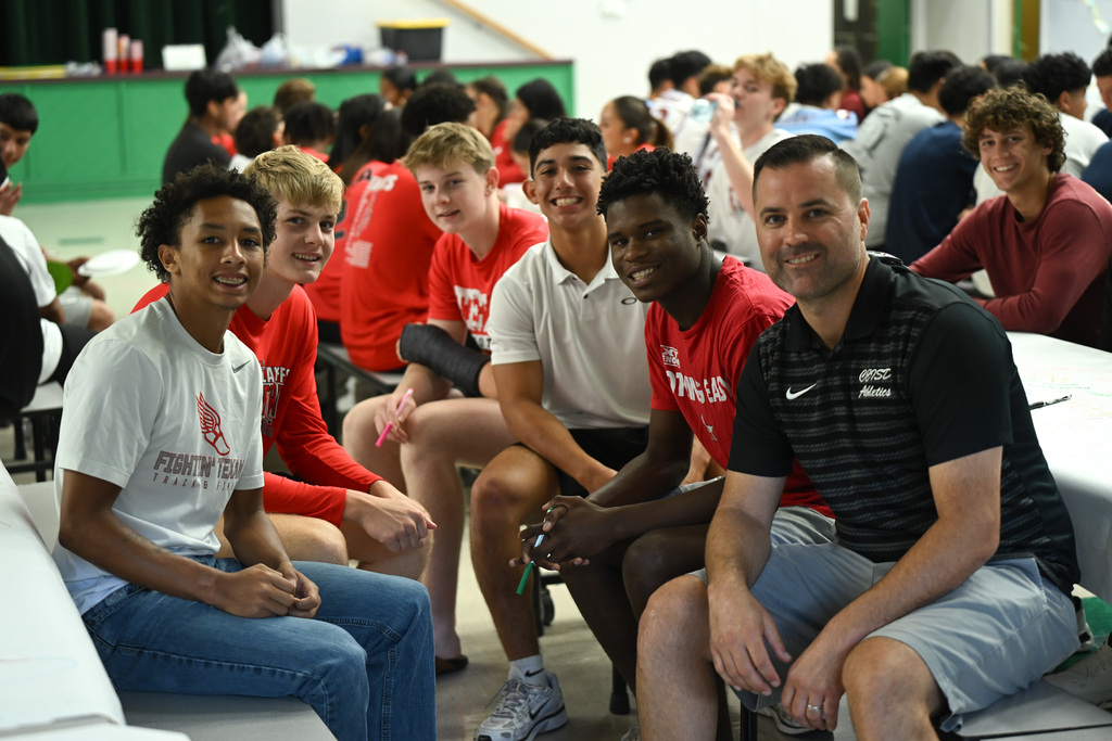 A group of young men wearing red, white, and black athletic shirts sitting on a bench.