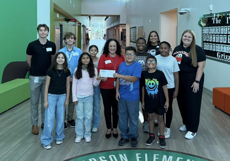 Group of students and teachers standing in a hallway; some wearing red shirts; one holding a certificate.