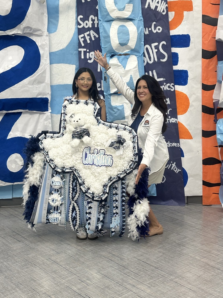 Two women standing in front of banners, one holding a large fluffy toy, both smiling.