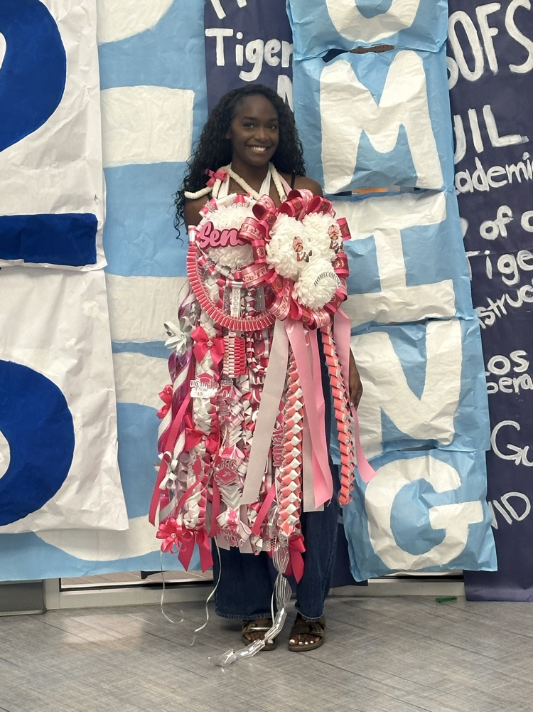Woman wearing a pink and white costume stands in front of a wall with blue and white signs.