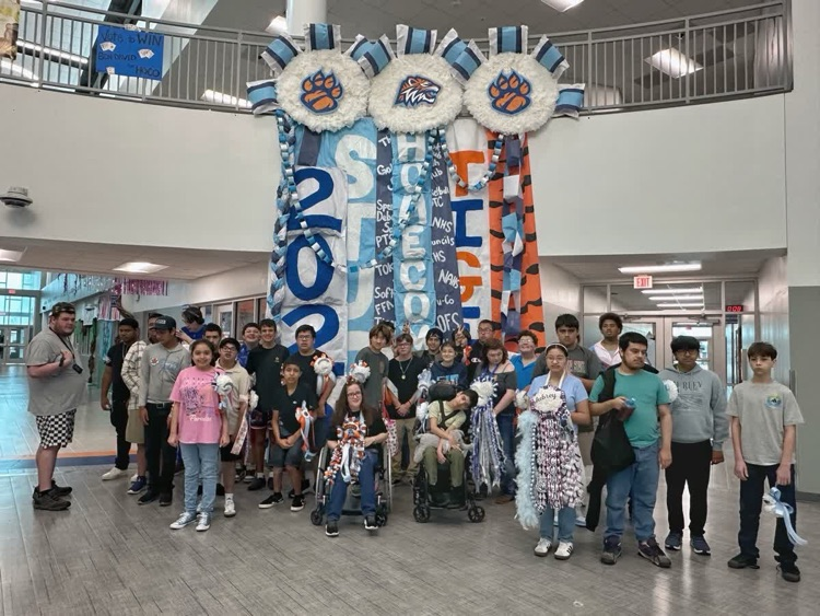 A group of students and staff pose for a picture in front of a decorated arch.