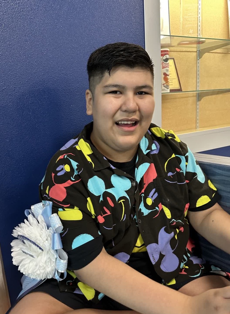 Teen in colorful shirt sits on couch with blue pillow and ribbon behind him.