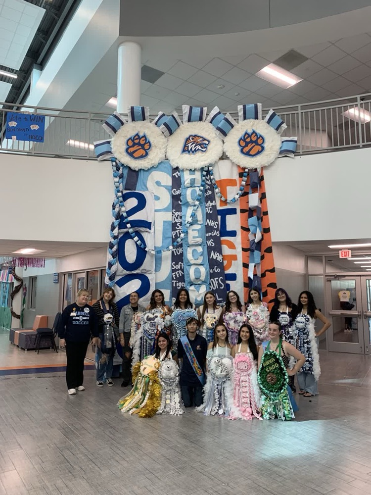 A group of students poses in front of a large display of banners with a paw print.