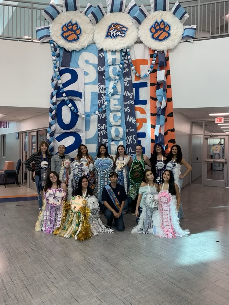 A group of students dressed in colorful costumes pose for a photo in front of a banner.