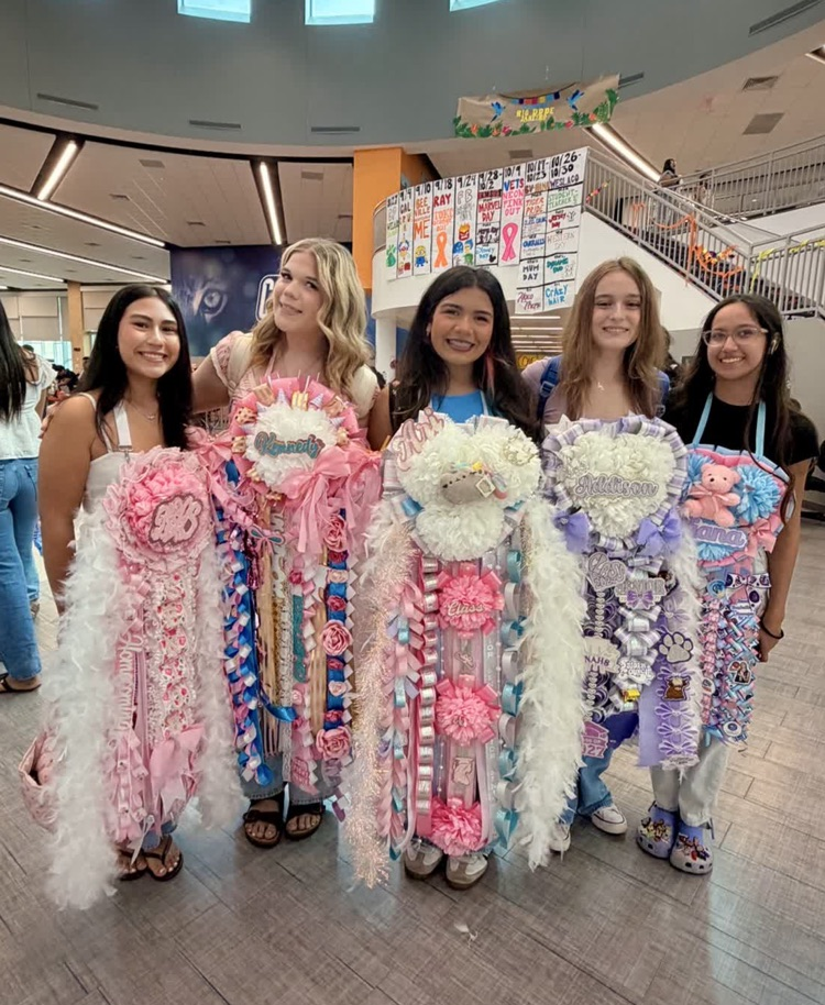 Five girls in front of a staircase. They are holding large decorations with feathers and ribbons.