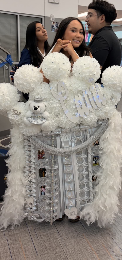 A woman stands in front of a large, white, feathery decoration, smiling. Two others stand behind her, one looking over the other's shoulder.
