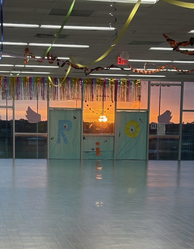 Empty room with large windows, colorful streamers, and a sunset view outside. Two painted doors with letters R and I.