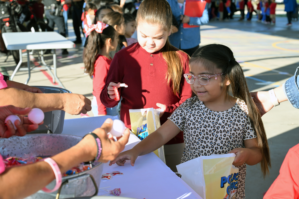 A group of children at a table with candy. A girl reaches for a bowl of candy while another holds a candy bag.