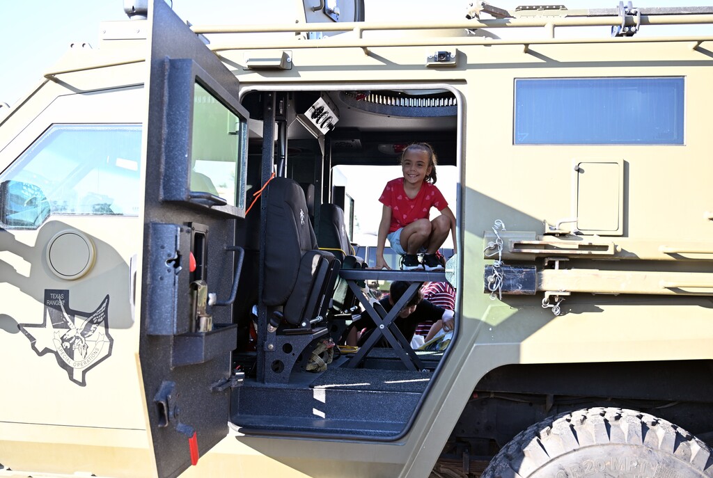 Girl sits in an open door of an armored vehicle, looking out from inside.