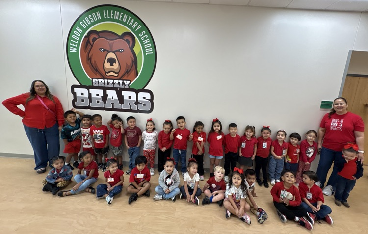 A group of young children and adults in red shirts pose for a photo near a wall.