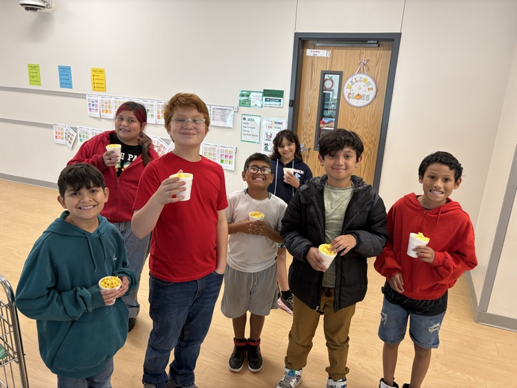 Group of students holding yellow cups with food inside, standing together in a room.