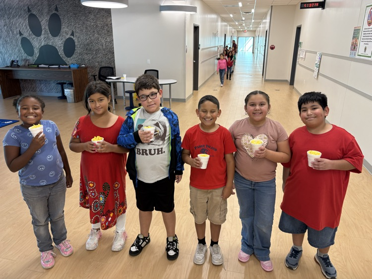 Seven children in a school hallway with yellow cups in their hands, smiling for the camera.