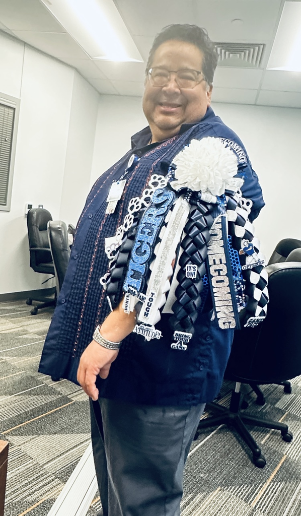 Man in an office with chairs and desk, wearing a blue jacket and a blue, white, and black pom-pom.