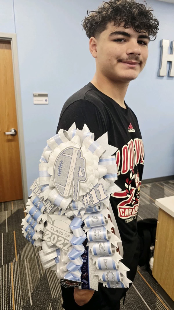 Teen holds pom-poms shaped as football in front of body. Pom-poms are blue and white.
