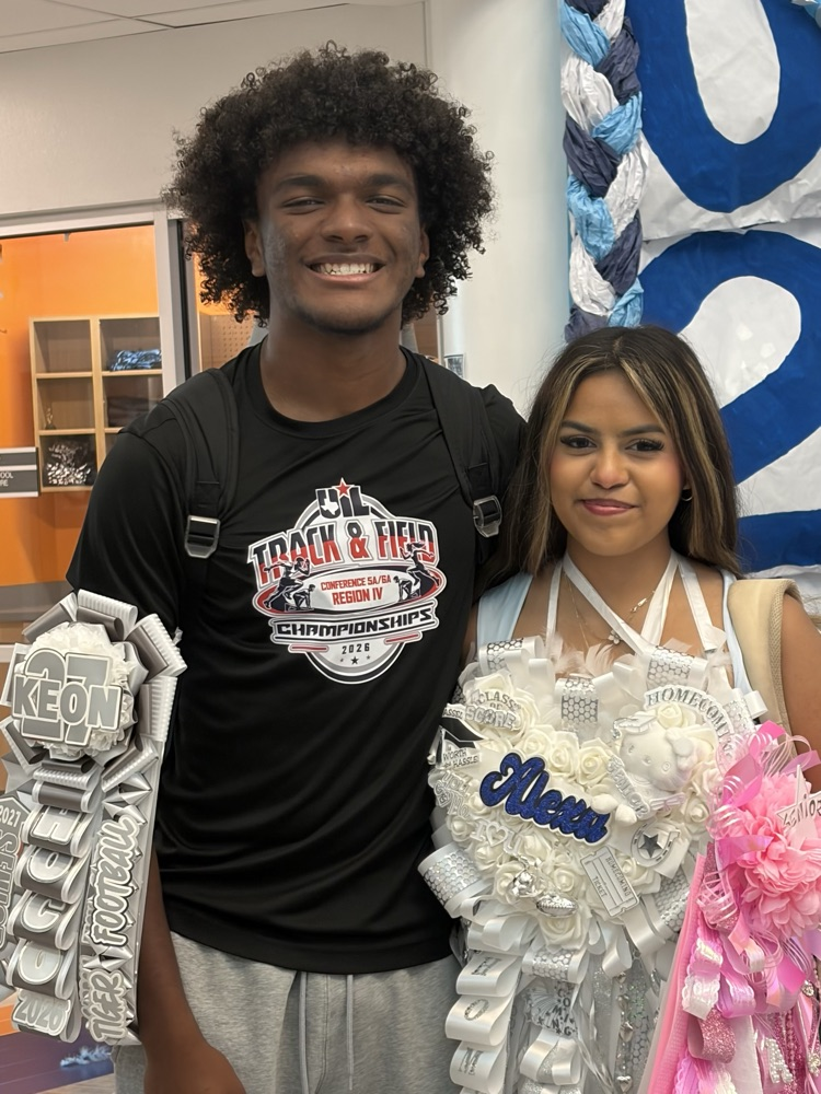 A smiling student in a black shirt with a backpack and a student with a pink sash.