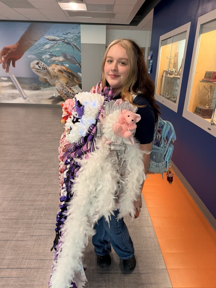 Girl in hallway holding white, multicolored scarf with plush toys, wearing jeans and black shoes.