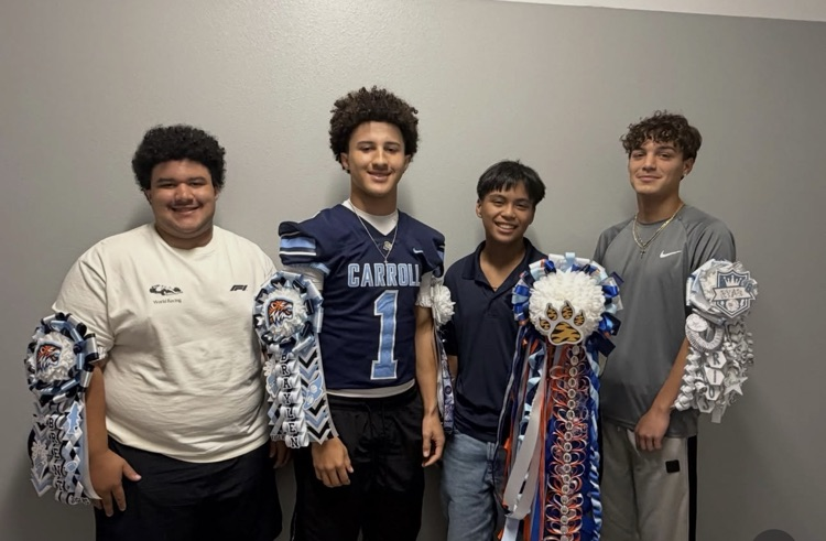 Five young men stand next to each other with a light-colored wall in the background, all holding pom-poms.