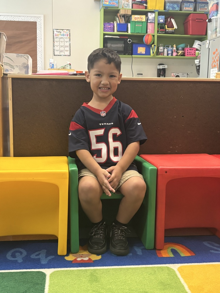 A young boy sits in a green chair wearing a football jersey with the number 56.