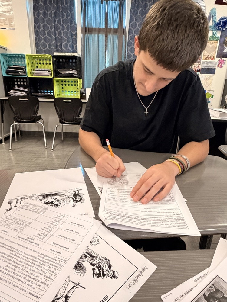 Two students seated at tables, one pointing at a paper with a pen, both 