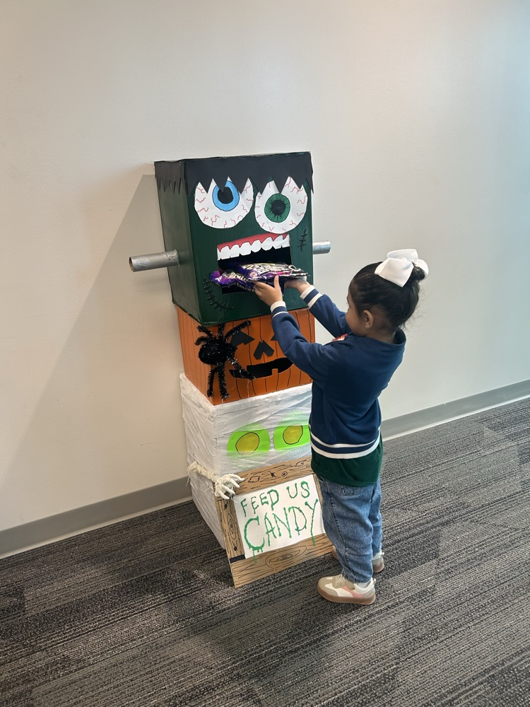 Child puts candy into a box with an animated mouth and eyes on a white wall.
