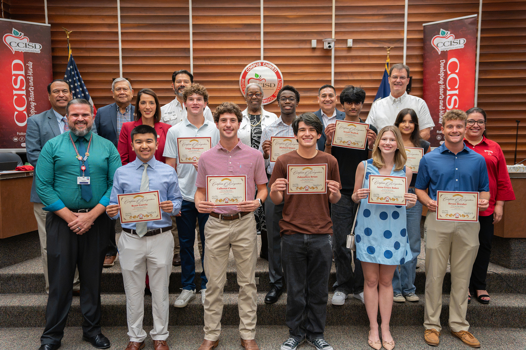 Group of students and adults holding certificates stand on a staircase in front of a wooden wall.