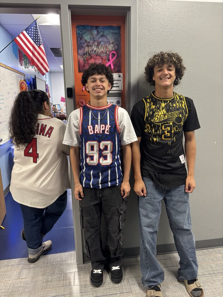 Three students stand near a door. One wears a basketball jersey with the number 93.