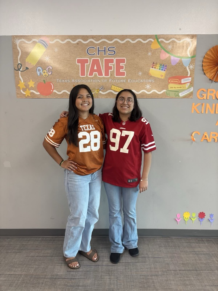 Two girls stand next to each other in a classroom. They wear jerseys with numbers 28 and 97. Behind them is a banner reading "CHS TAFE."