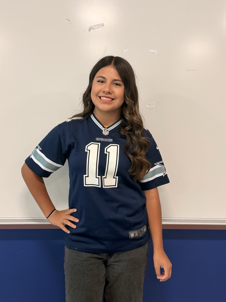 A girl in a blue sports jersey with white numbers 11 stands in front of a white board.