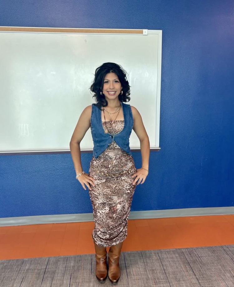A woman stands with hands on hips in a room. A white board is on the wall behind her.