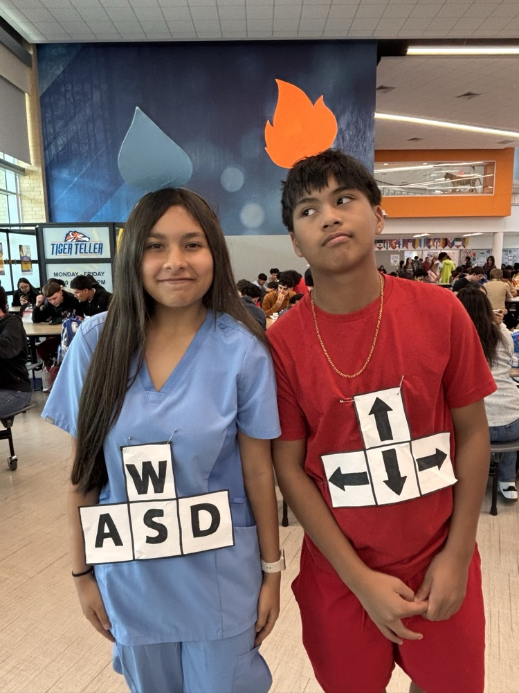 Two children in costumes pose in a cafeteria. One wears blue with a sign that says WASD.