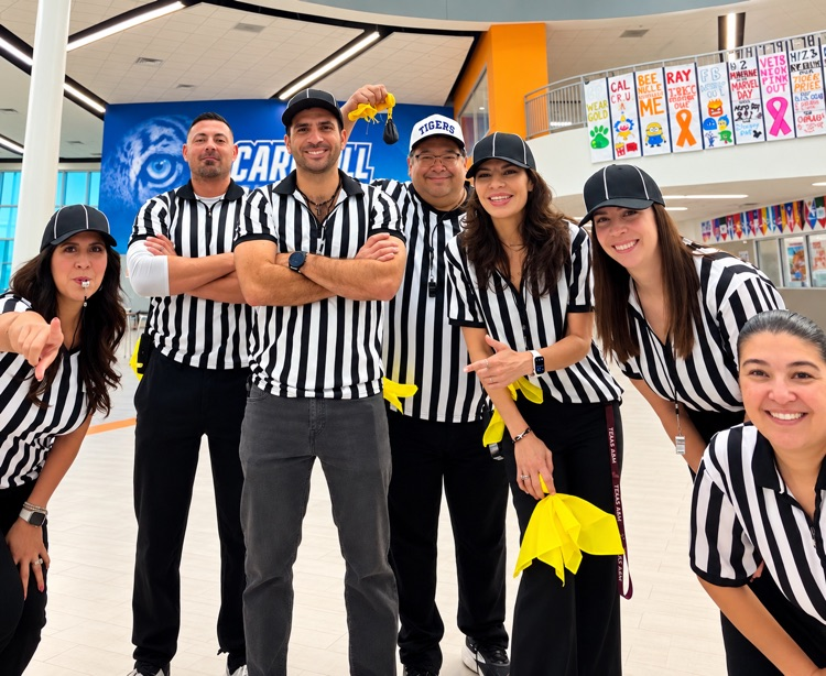 Nine adults in striped uniforms posing for a photo inside a hallway with glass railings.