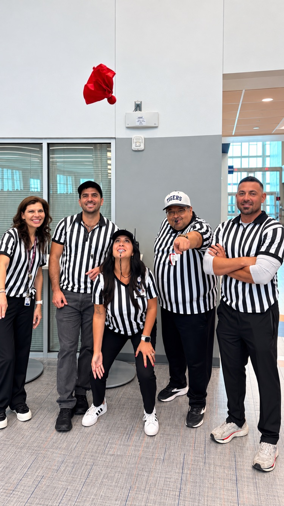 Five people in black and white striped shirts posing for a photo in a school hallway.