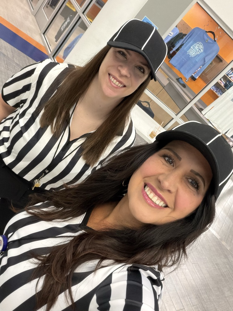 Two women with long hair wear black and white striped uniforms and black caps. They stand together and smile at the camera.