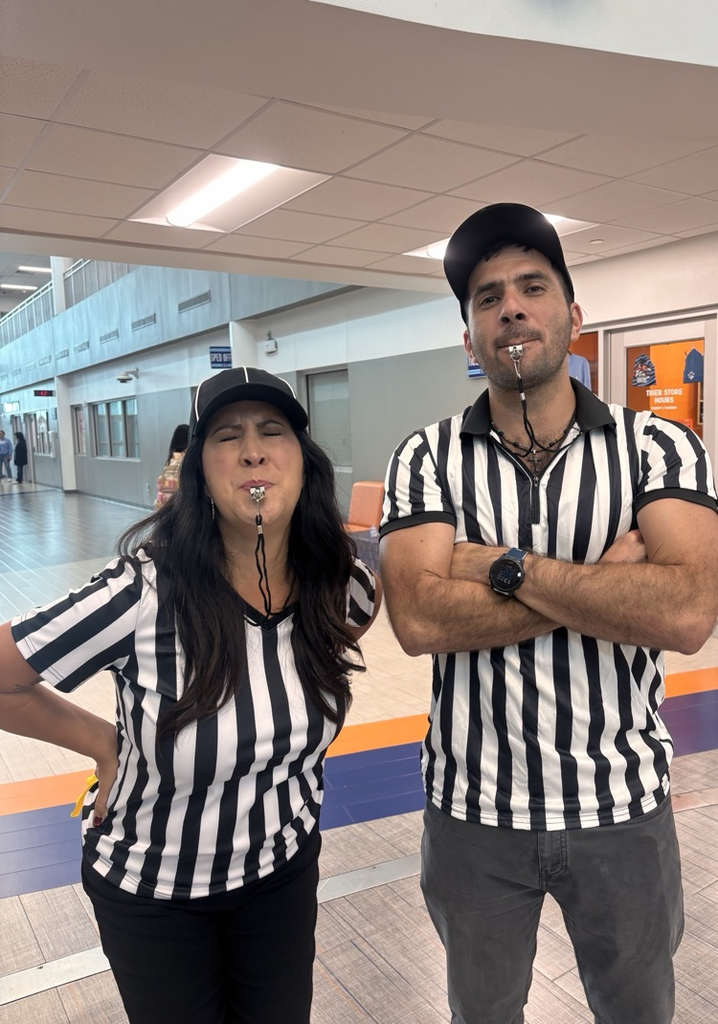 A man and woman in matching striped shirts, both with whistles around their necks, pose with their hands on their hips.