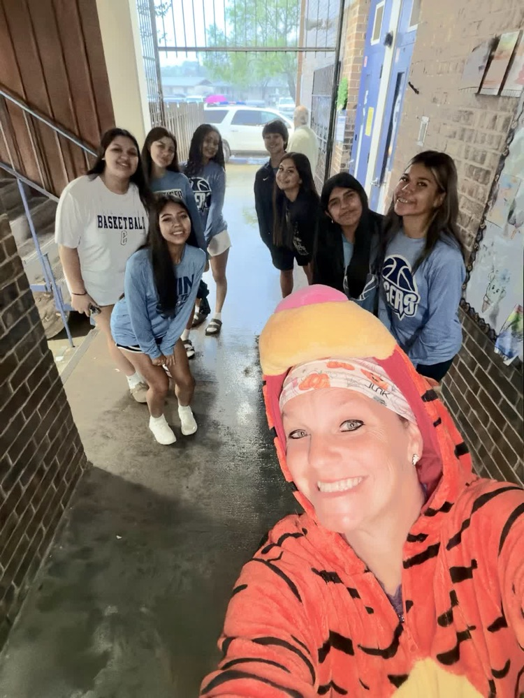 A group of students in blue jackets stands in a hallway, one taking a selfie.