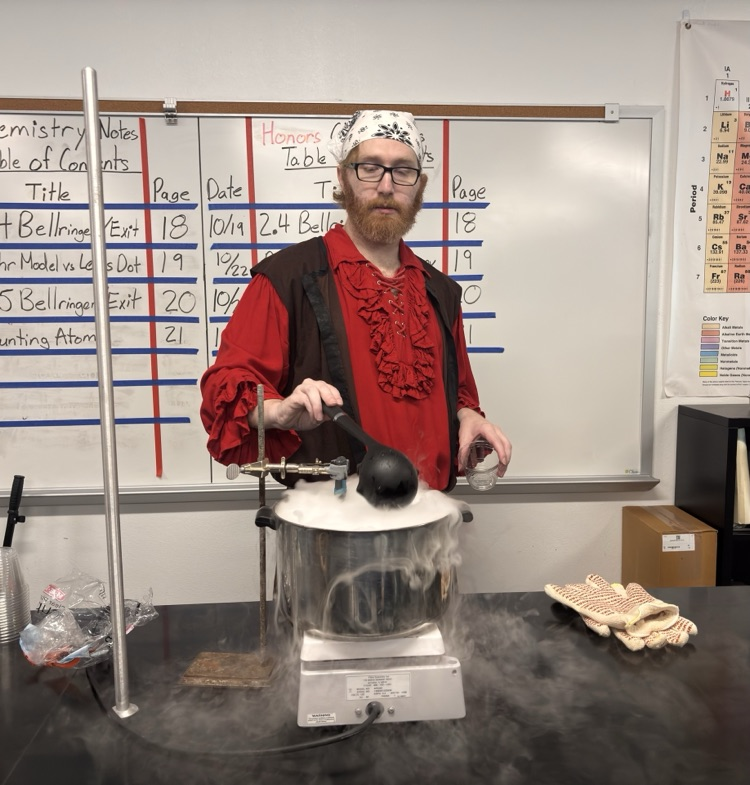 A person wearing a red shirt and a white bandana stands before a table with a boiling pot.