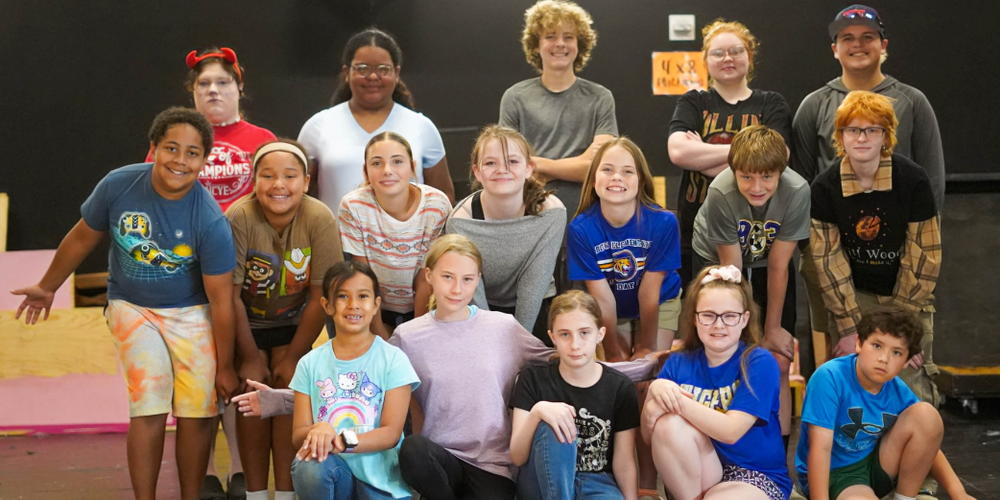 Group of children posing together on a stage, arranged in rows and facing the camera.