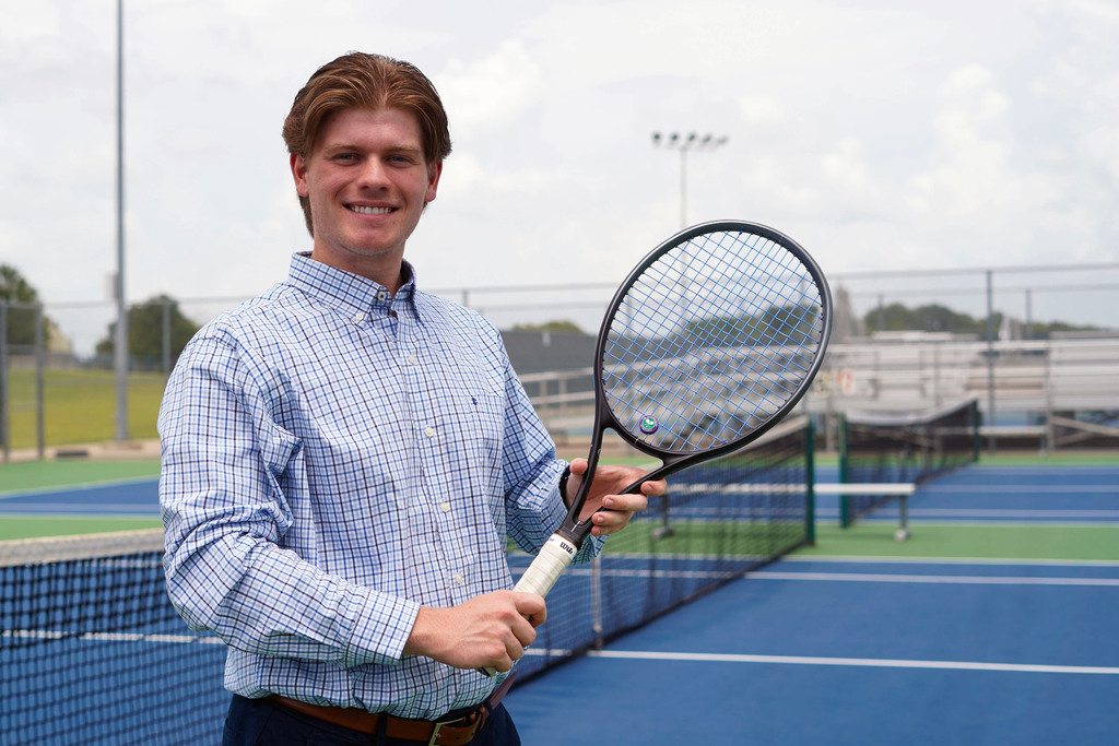 well dressed man holds tennis racquet