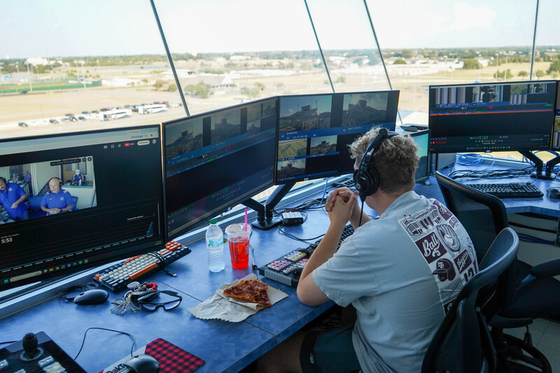Control room atop Community National Bank & Trust Stadium buzzes with activity as crews run cables, cue graphics, and check audio.