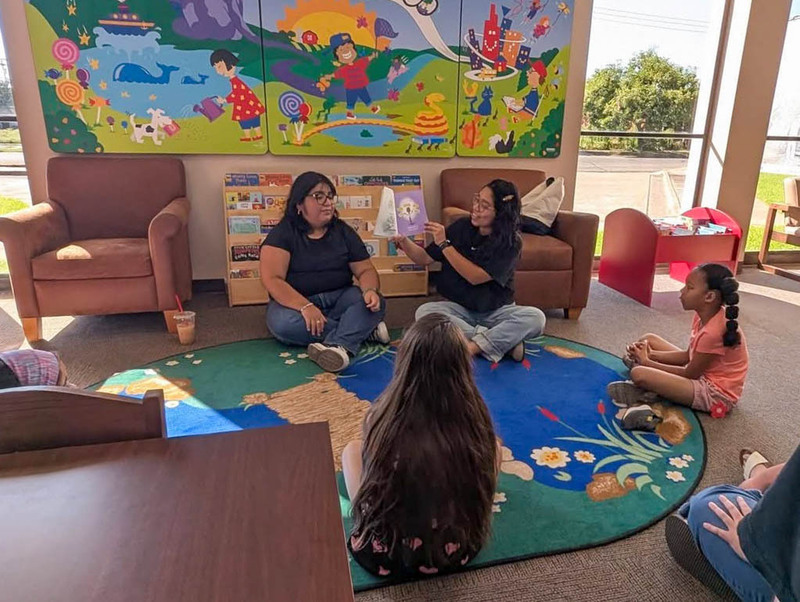 Corsicana ISD teacher gathered around a table in a library during a bilingual reading activity