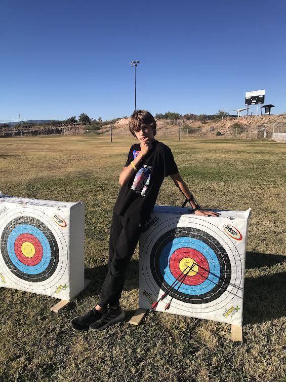 Male student posing in front of a target with 3 arrows in the yellow area