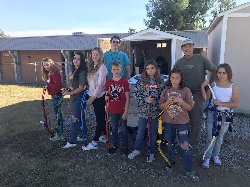 Students and instructors standingin front of storage shed with bows in front of them