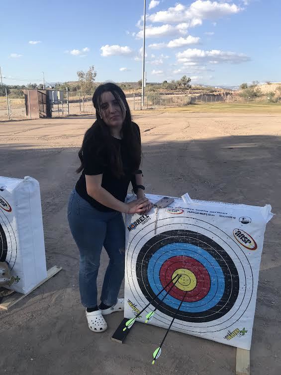 Female student standing by a target with 3 arrows in the yellow