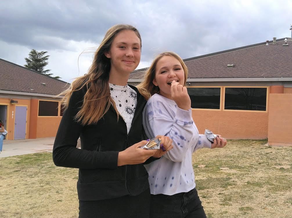 Two Smiling female students with almond package and one biting an almond
