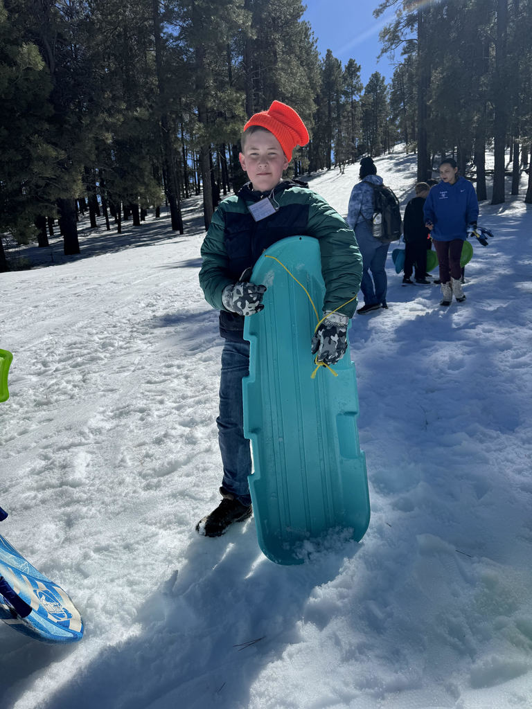 Boy holding snowsled on snowy slope with 3 onlooers